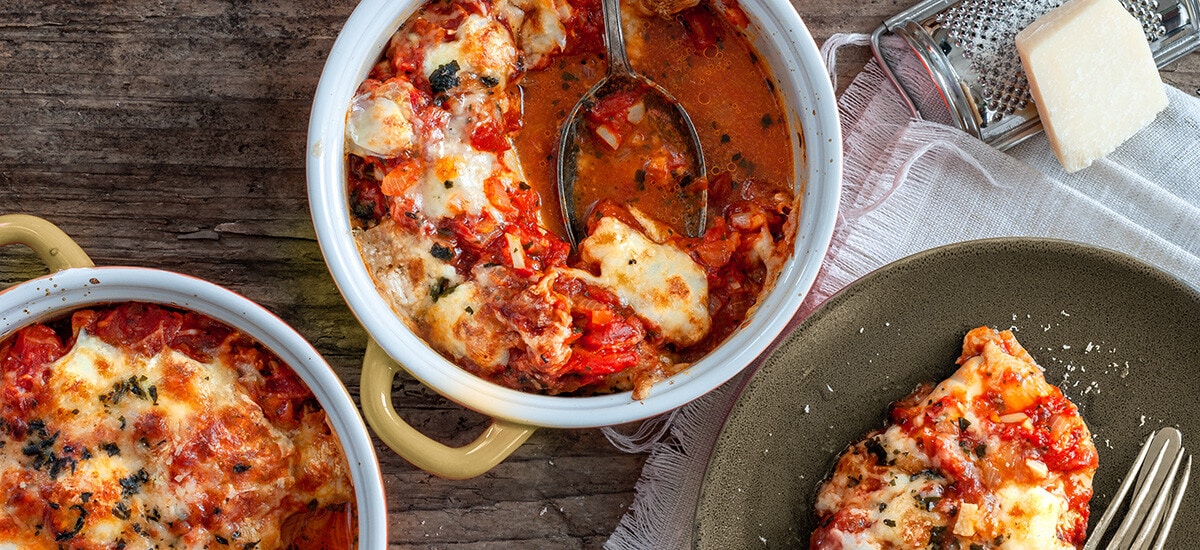 2 kleine Ofenformen mit Hühnchen in Tomatensauce und Mozzarella mit einem Teller.