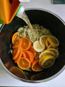 In Topf mit Holunderblüten und Orangen- und Zitronenscheiben wird Saft geschüttet