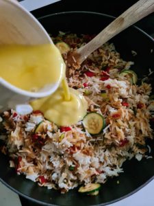 Flüssiges Ei wird in Gemüse-Reis-Pfanne geschüttet