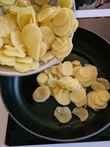 Kartoffelscheiben werden in Pfanne gegeben